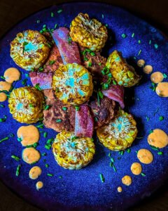 chicken breast wrapped in bacon with corn on the cob pieces and sauce on a place.