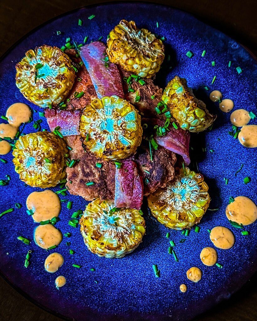 chicken breast wrapped in bacon with corn on the cob pieces and sauce on a place.