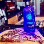 iberico pork on a wooden cutting board next to a bottle of blue illuminated tequila.