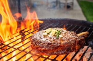 Ribeye Steak with herb butter on top with flames on grill